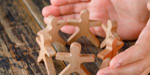 Business success concept on wooden background high angle view. hands protecting wooden figures of people.