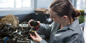 Attentive female mechanic holding spare parts of car at repair garage